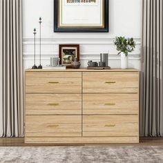 a wooden dresser sitting in front of a window with curtains on either side and a framed picture above it