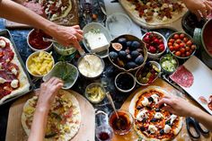 a group of people making pizzas at a table with bowls and pans full of food