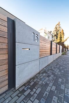 the number fifteen is on the concrete wall next to the brick sidewalk and trees in the background