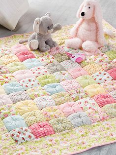 two stuffed animals sitting on top of a quilt