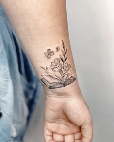 a woman's arm with a book and flowers tattoo on her left wrist,