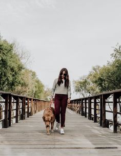 a woman walking her dog across a wooden bridge