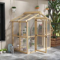 a small wooden greenhouse sitting on top of a stone floor next to a tree and potted plants