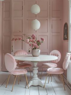 a white table with pink chairs and flowers in a vase on top of it, next to a radiator