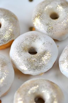 four donuts with white frosting and gold sprinkles on a plate