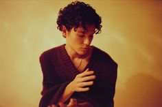 a man with curly hair wearing a black sweater and listening to his cell phone while standing in front of a yellow wall