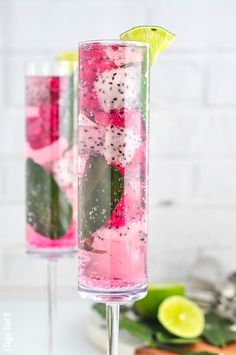 two tall glasses filled with pink and green drinks on top of a white table next to lime slices