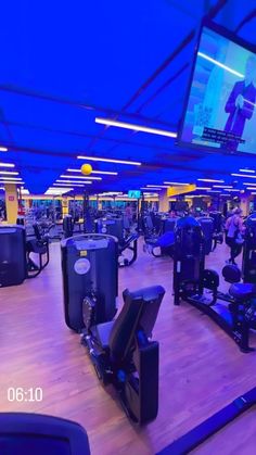 an indoor gym with many machines and people watching televisions on the wall behind them