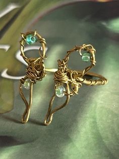 two gold rings with green glass beads on top of a leafy table next to an object