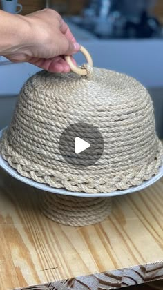 a person is holding a rope covered hat on a wooden table with other items in the background