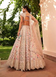 a woman in a white and pink lehenga with floral embroidery on the back