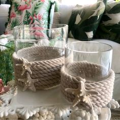 two glass cups with seashells and starfish decorations on a tray in front of a couch