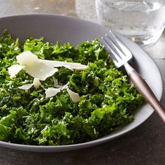 a white plate topped with green vegetables next to a glass of water and a fork