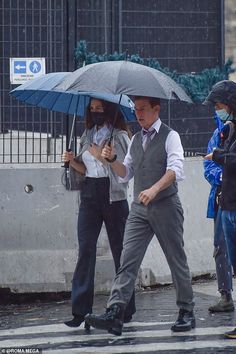 two people walking in the rain with umbrellas over their heads and one person holding an umbrella