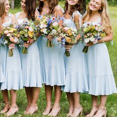 a group of women standing next to each other in front of a field holding bouquets