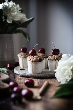 small cupcakes with cherries and nuts on a plate next to some flowers