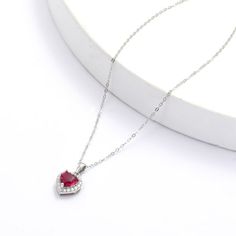 This rhodium over sterling silver pendant features a 7x7 mm heart shaped lab created ruby in the center accented with 28 pieces of round cut moissanite stones of 1.4 mm around the main stone creating a halo necklace design. Cubic Zirconia Heart Necklace With Gemstone For Valentine's Day, Heart Necklace With Cubic Zirconia For Valentine's Day, Valentine's Day Heart Necklace With Cubic Zirconia Gemstone, Cubic Zirconia Gemstone Heart Pendant Necklace, Heart-shaped Lab-created Ruby Birthstone Jewelry, Red Cubic Zirconia Heart Pendant Jewelry, Heart-shaped Lab-created Ruby Gemstone Jewelry, Valentine's Day Diamond Heart Necklace With Gemstone, Silver Gemstone Heart Necklace For Valentine's Day