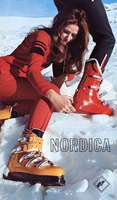 a woman sitting in the snow with skis on her feet and wearing red pants