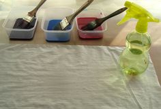 three plastic containers filled with different types of paint and two wooden spoons sitting on top of a table