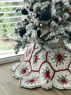 a crocheted christmas tree skirt sits on the floor in front of a window