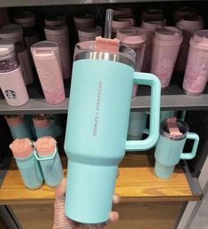 a person holding a blue coffee cup in front of many cups and mugs on shelves