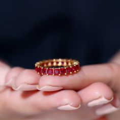 a close up of a person's hand holding a gold ring with red stones