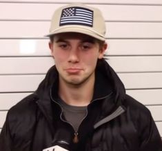 a young man wearing a hat and holding a microphone in front of a white wall