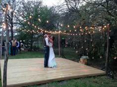 a bride and groom dance on a deck surrounded by string lights