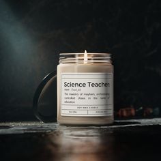 a candle sitting on top of a wooden table next to a black mug with the words science teacher written on it