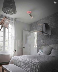 a white bed sitting next to a window in a bedroom under a light fixture with flowers hanging from the ceiling