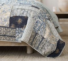 a bed with a blue and white quilt on it's coverlet next to a nightstand