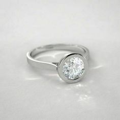 a white gold engagement ring with a round diamond in the center on a plain surface