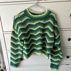 a green and white knitted sweater hanging on a clothes hanger next to drawers