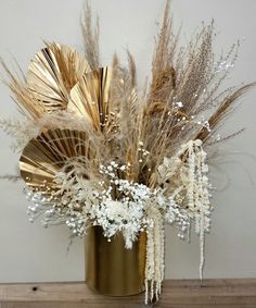 a gold vase filled with lots of dried flowers and feathers on top of a wooden table