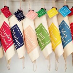 several different colored tea towels hanging from hooks on a wall with name tags attached to them