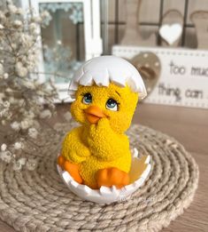 a yellow toy duckling sitting in an egg shell on a table next to a white flower