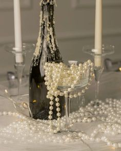 a table topped with a bottle of wine and two glasses filled with pearls next to candles