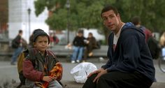 a man sitting next to a little boy on the side of a road with other people