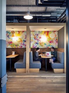 two people sitting at a table in an office with colorful paintings on the wall behind them