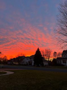 the sun is setting over some houses and trees in front of a red cloudy sky