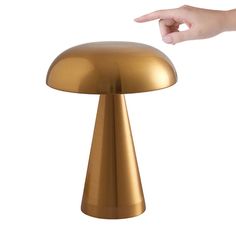 a gold mushroom shaped table lamp with one hand reaching for the light on it's base