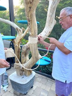 two men are standing next to a tree that is made out of driftwood and rope