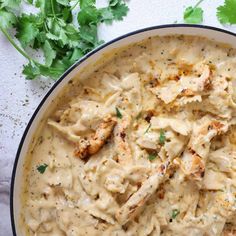 a white bowl filled with chicken and gravy next to cilantro leaves