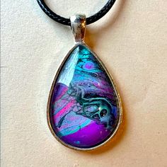 a necklace with a purple and blue tear shaped pendant hanging from a black leather cord