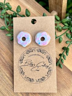 two pink donuts with sprinkles are on a brown card next to some green leaves