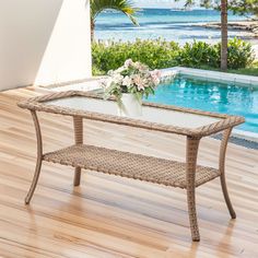 a glass table with flowers on it in front of a swimming pool and palm trees