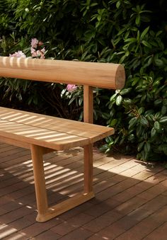 a wooden bench sitting on top of a brick floor next to green bushes and flowers