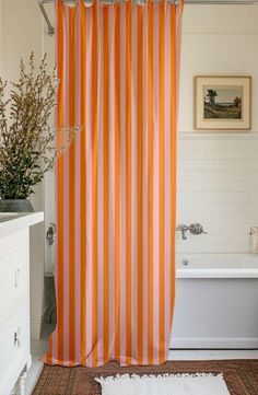 an orange and white striped shower curtain next to a bathtub with a rug on the floor