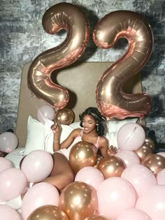 a woman sitting in bed surrounded by balloons with the number twenty two on it's side