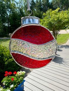 a red and white ornament hanging from a string on a wooden deck next to flowers